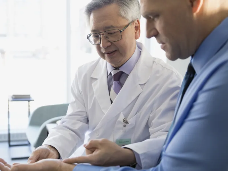 An Asian doctor identifies pain points on a male patient.