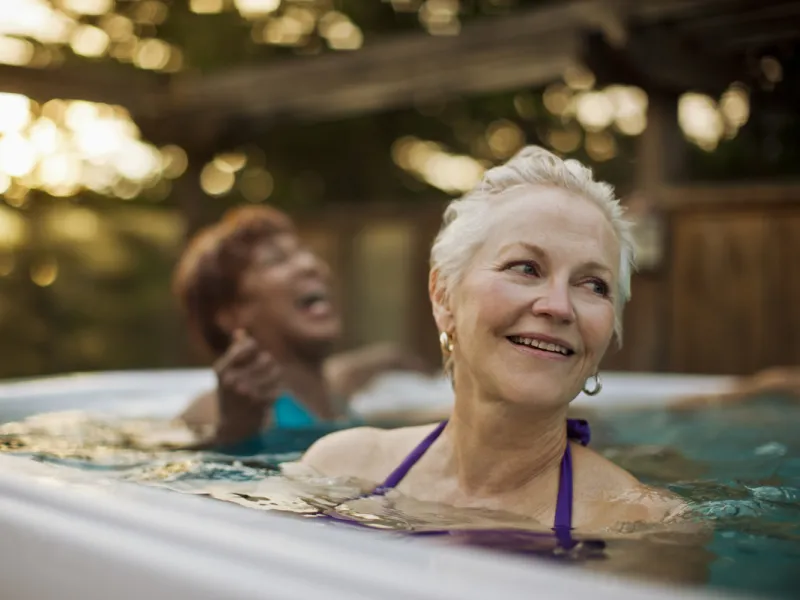 Two women laugh while soaking in an outdoor spa
